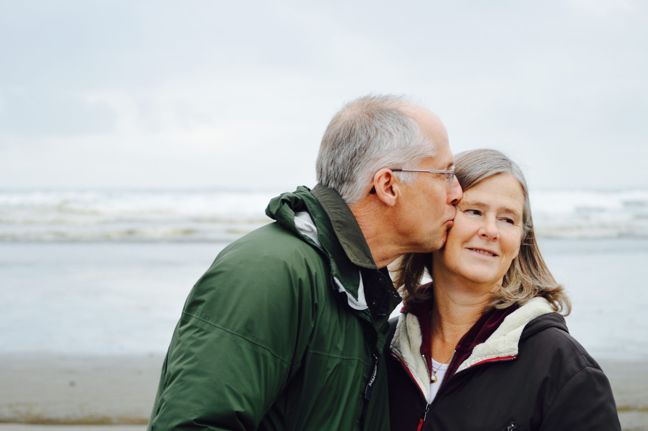 An elderly couple being affectionate at the beach.