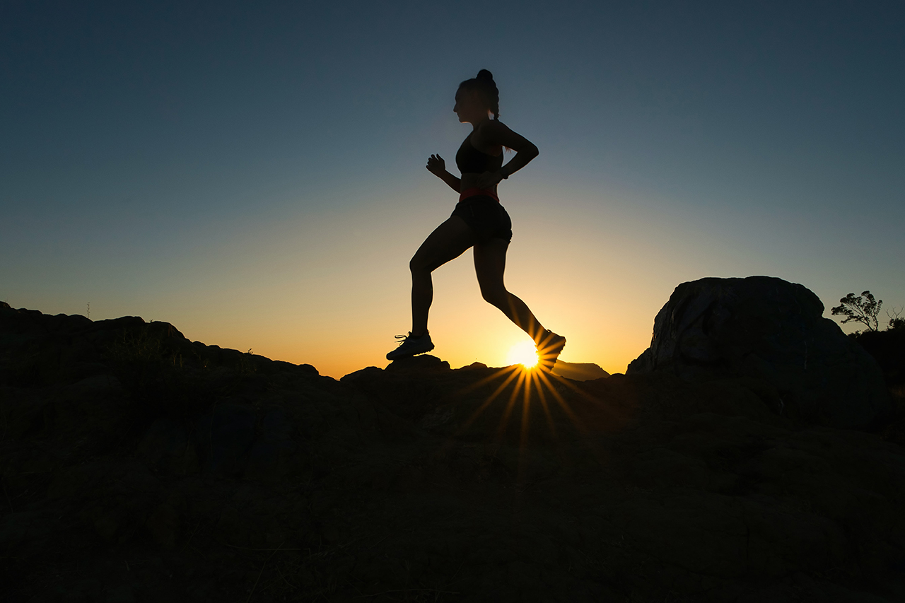 A silhouette of a woman running in front of a sunset along a ridge.